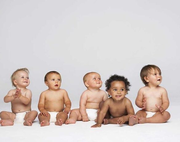 Five diverse babies sitting on a neutral background, displaying playful expressions