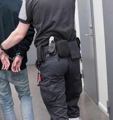 Officer escorting handcuffed person down hallway.