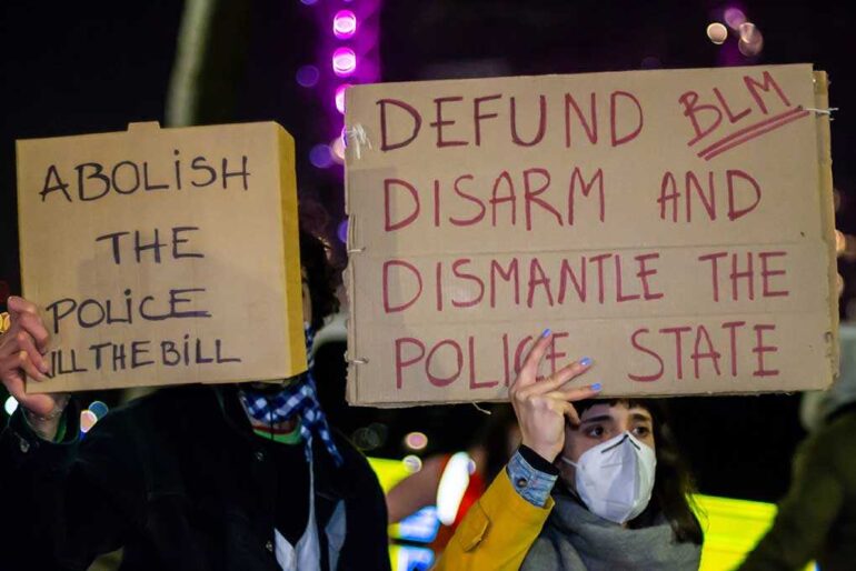 Two individuals holding protest signs with messages about police reform