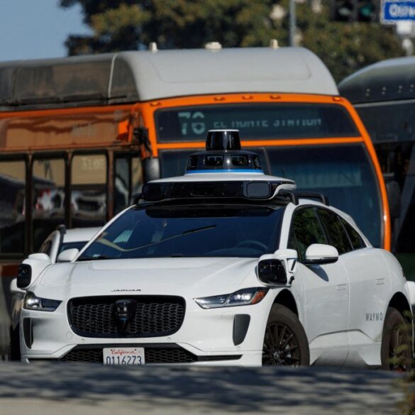 A white Waymo driverless car in traffic in downtown Los Angeles.