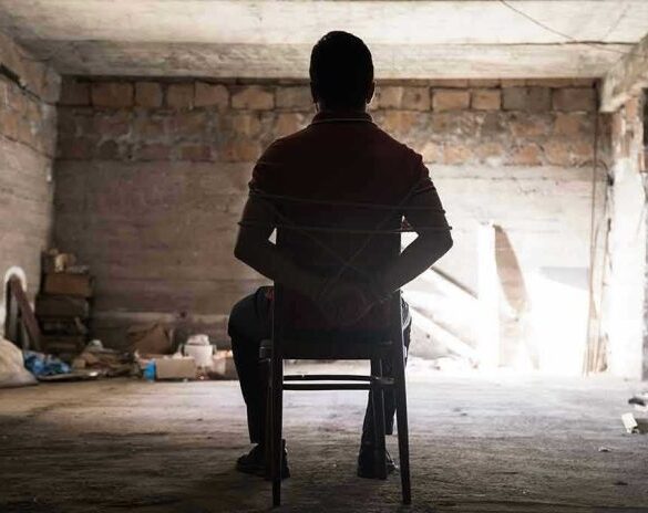 Person tied to chair in dimly lit room.