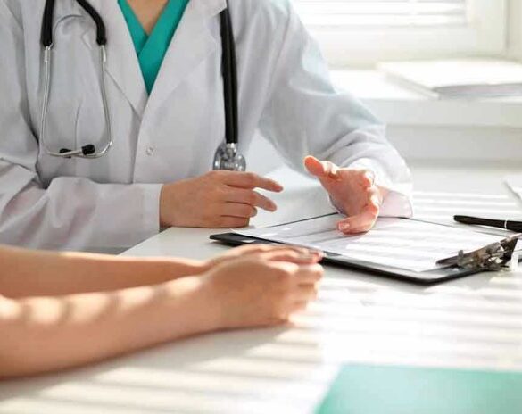 Doctor discussing with patient, holding clipboard on desk.
