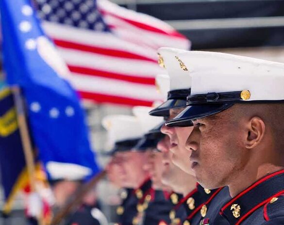 Marines in uniform standing in formation with flags in the background