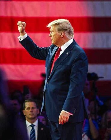 Person in suit with fist raised in front of flag.