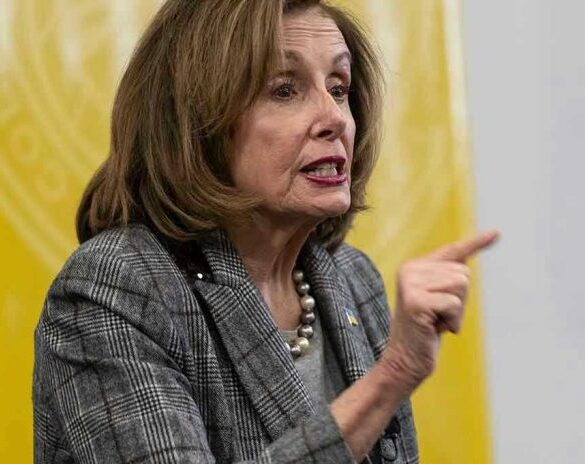 Woman speaking and pointing, wearing a plaid jacket.