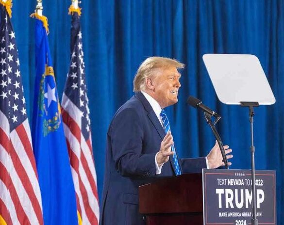 Person speaking at podium with flags in background.
