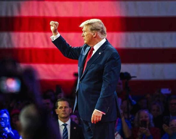 Person in suit with fist raised in front of flag.