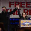 Zohran Mamdani and Kathy Hochul raise joined hands, with other politicians, in front of a "New York is Not For Sale" banner.