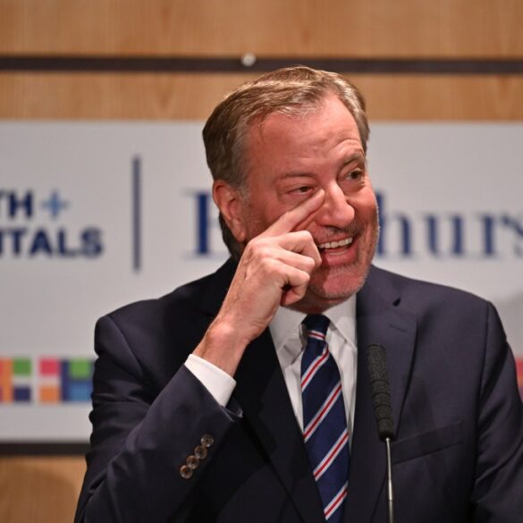 Former NYC Mayor Bill de Blasio touching his nose while speaking at an event.