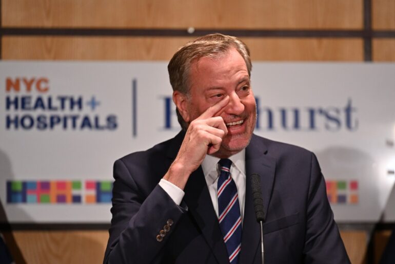 Former NYC Mayor Bill de Blasio touching his nose while speaking at an event.