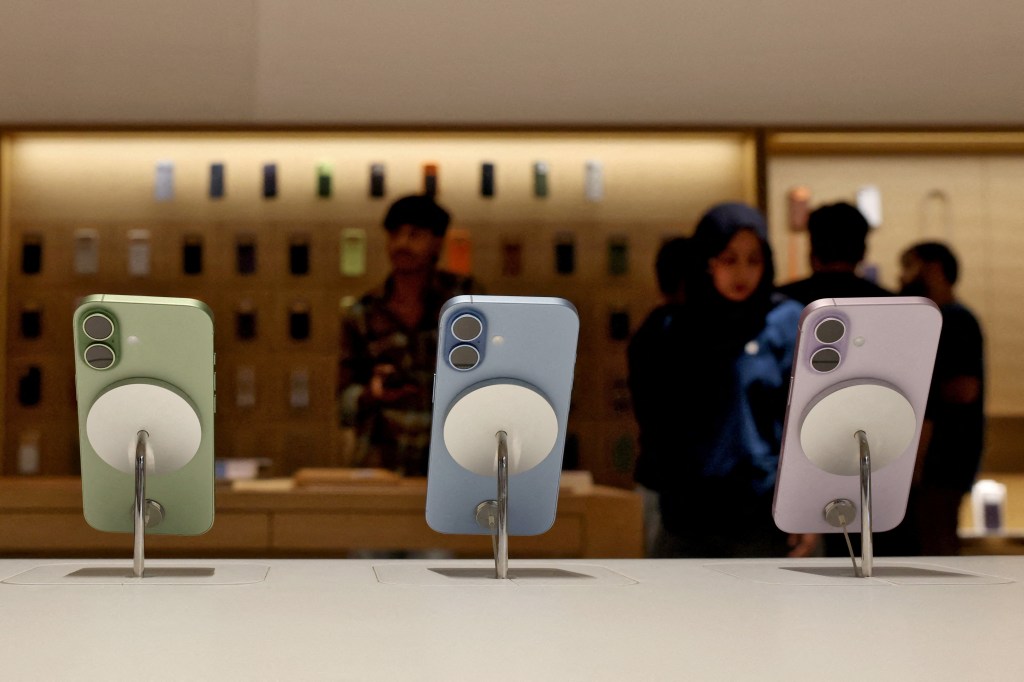 Three iPhone 17 phones, light green, light blue, and light purple, on display at an Apple store.