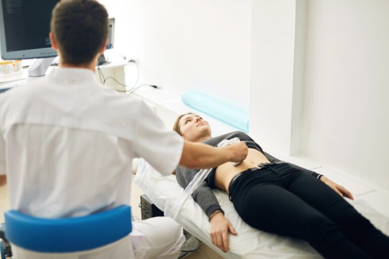 A medical professional performing an ultrasound on a woman's abdomen.