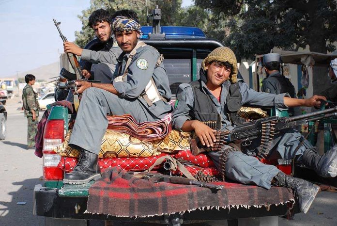 Three armed soldiers sitting on the back of a military vehicle in an urban setting