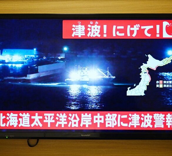 TOPSHOT - An advisory reading "Tsunami! Run!" (top) and "Tsunami warning issued for central Hokkaido's Pacific Coast" flashes over the live footage of a boat leaving a port, on a television screen in Sapporo, in Japan's northern Hokkaido prefecture on December 8, 2025. Japan recorded a 40-centimetre (16-inch) tsunami after a 7.6-magnitude quake on December 8. (Photo by GREG BAKER / AFP via Getty Images)