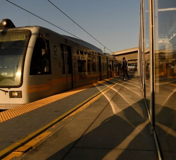 Transit passengers wear face masks as they wait to board the Metro C Line, formerly Green Line, light rail train alongside the 105 Freeway at the Judge Harry Pregerson Interchange during rush hour traffic in Los Angeles, California on July 16, 2021. - The Metro C Line will eventually merge with the Crenshaw/LAX Transit Project as infrastructure modernization and transit construction projects continue at the airport ahead of the 2028 Los Angeles Olympics to reduce carbon emissions, traffic, and their impact towards climate change. (Photo by Patrick T. FALLON / AFP) (Photo by PATRICK T. FALLON/AFP via Getty Images)