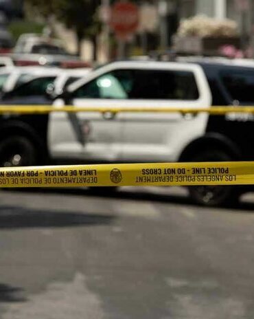 Police tape blocking street with patrol cars.