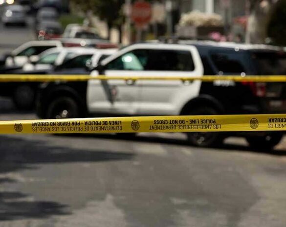 Police tape blocking street with patrol cars.