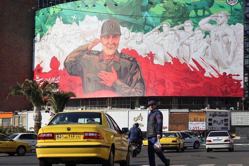 Iranians ride their motorbike past a huge banner of former Iran Islamic Revolutionary Guard Corps (IRGC) Quds Force commander Qasem Soleimani ahead of the sixth anniversary of his assassination Iraq, at Valiasr Square in Tehran, on December 31, 2025. Soleimani was killed on January 3, 2020, in a targeted US airstrike at Baghdad airport in Iraq. (Photo by ATTA KENARE / AFP via Getty Images)