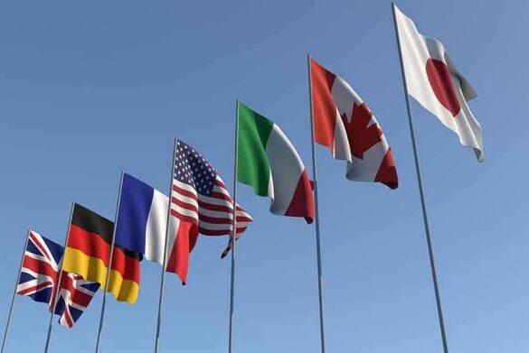 Flags of seven countries against clear blue sky.