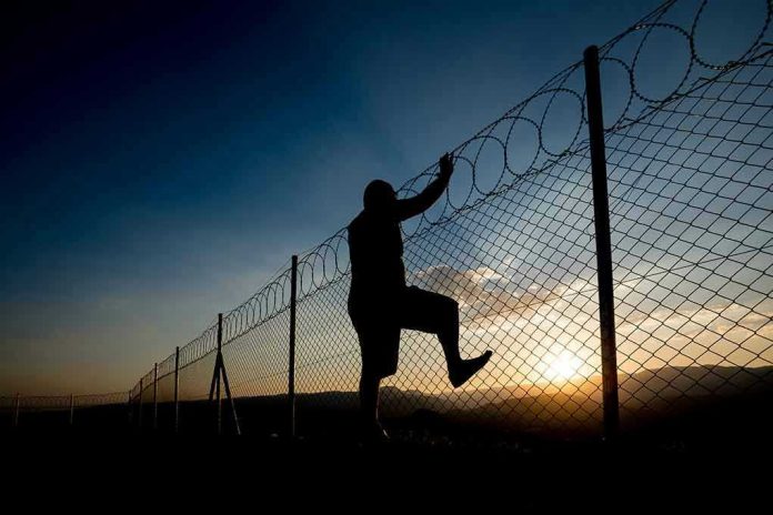 Silhouette of person climbing barbed wire fence at sunset.