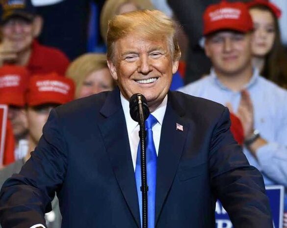 Man in suit speaking at rally with red hats.
