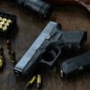 Handgun with ammunition, magazine, and rifle on wooden table.