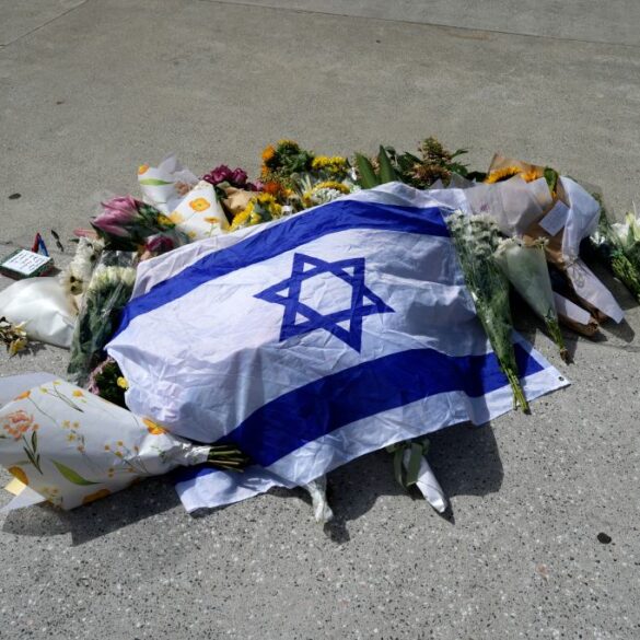 An Israeli flag laid on the ground amongst flowers, tributes, and a small notebook with pens.