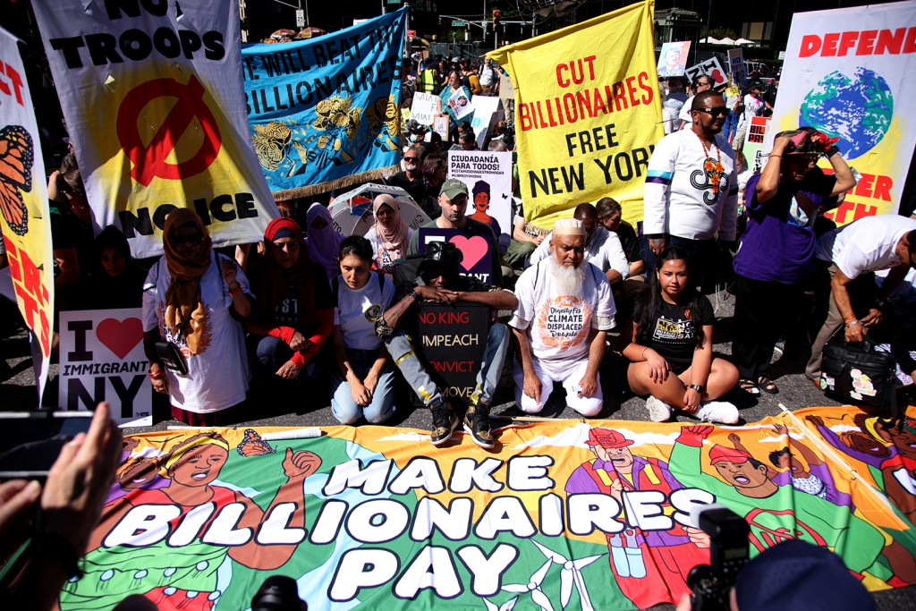 People protesting with signs and banners reading "Cut Billionaires Free New York," "No Troops No War Noice," "Defend Earth," and "Make Billionaires Pay."