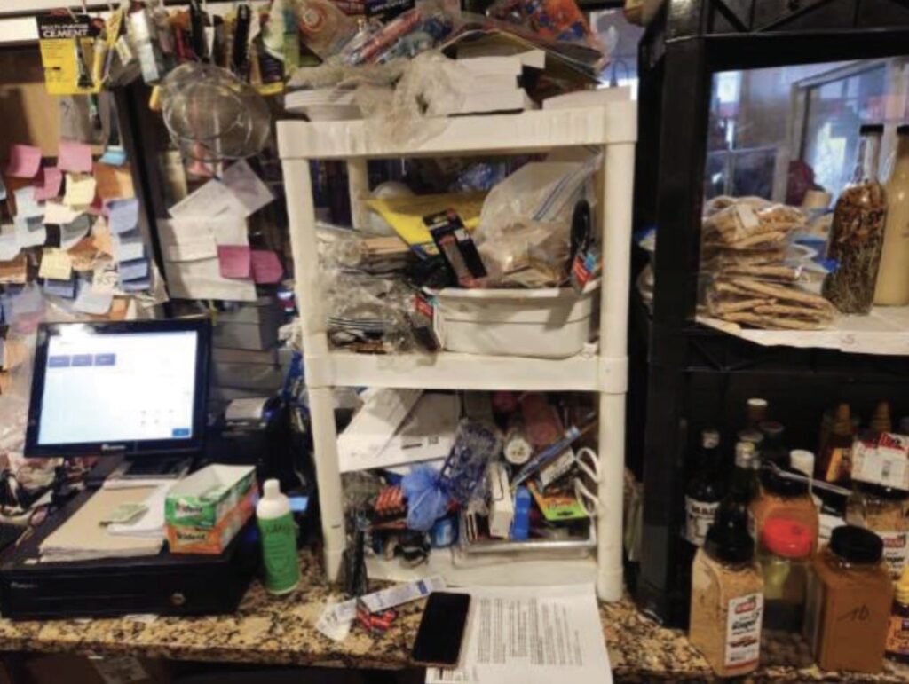 Cluttered checkout area featuring a computer, shelves filled with assorted items, and numerous sticky notes on the wall.