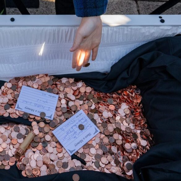 An attendee throws a penny into the casket at the "funeral for the penny," months after President Trump's administration ordered the Treasury Department to halt production of the coins, at the Lincoln Memorial in Washington, D.C., U.S., December 20, 2025.