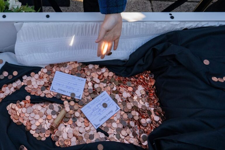 An attendee throws a penny into the casket at the "funeral for the penny," months after President Trump's administration ordered the Treasury Department to halt production of the coins, at the Lincoln Memorial in Washington, D.C., U.S., December 20, 2025.