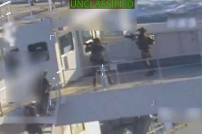 A video still showing soldiers with rifles on a boat, with the word "UNCLASSIFIED" at the top.