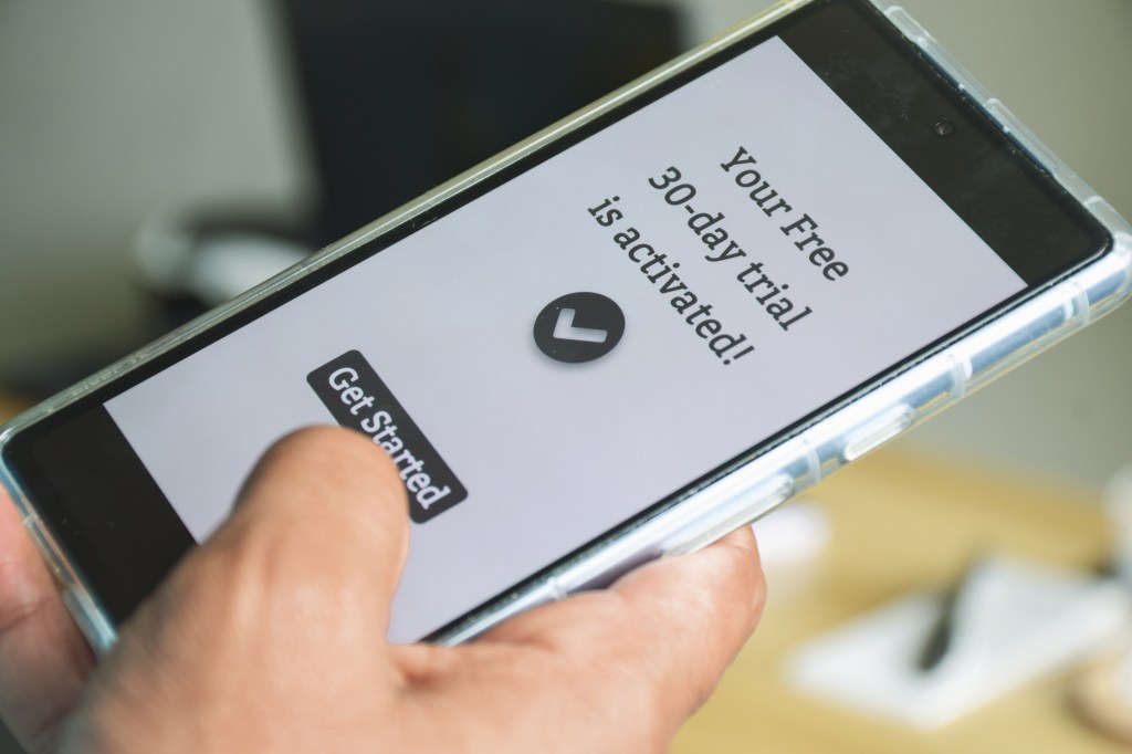 Hand holding a smartphone with "Your Free 30-day trial is activated!" and a "Get Started" button on the screen.