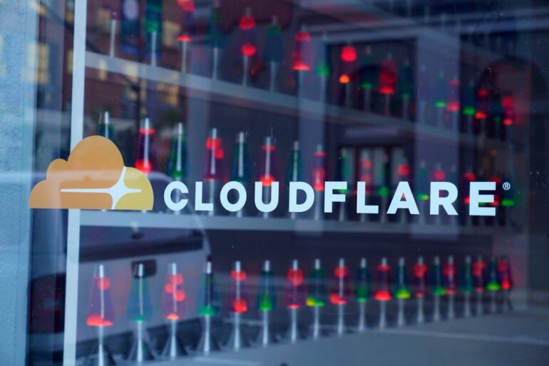The Cloudflare logo on a window with many red and green lava lamps inside.