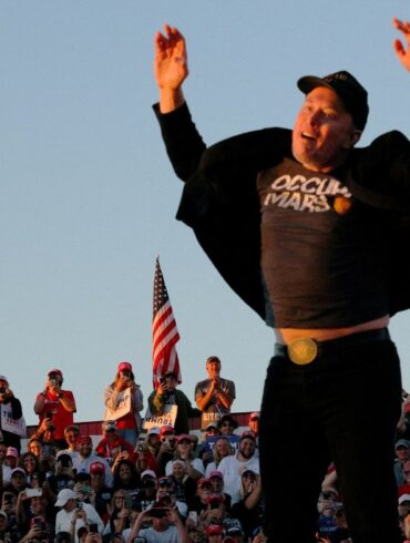 Elon Musk reacts while standing next to Donald Trump at a rally.