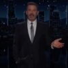 Jimmy Kimmel standing in front of a city skyline at night, gesturing with his right hand.
