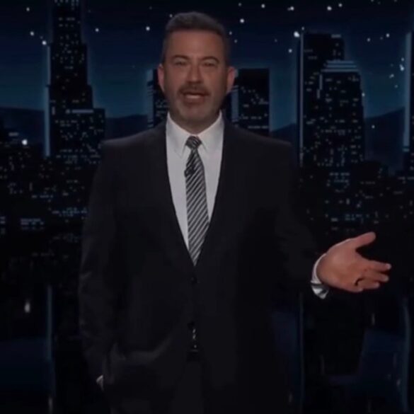 Jimmy Kimmel standing in front of a city skyline at night, gesturing with his right hand.