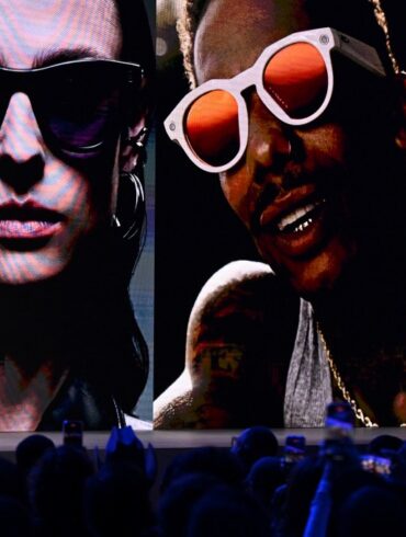 Mark Zuckerberg on stage with large images of people wearing smart glasses behind him.