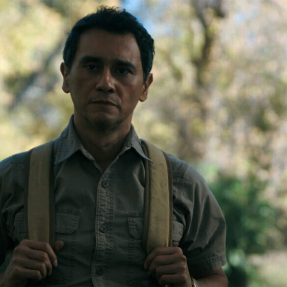 Manousos holding onto his backpack straps in the jungle in Pluribus episode 7