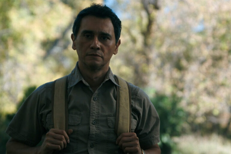 Manousos holding onto his backpack straps in the jungle in Pluribus episode 7