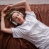 Woman relaxing and listening to music using headphones while lying in bed.