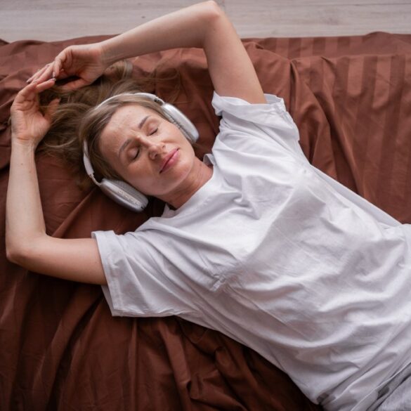 Woman relaxing and listening to music using headphones while lying in bed.