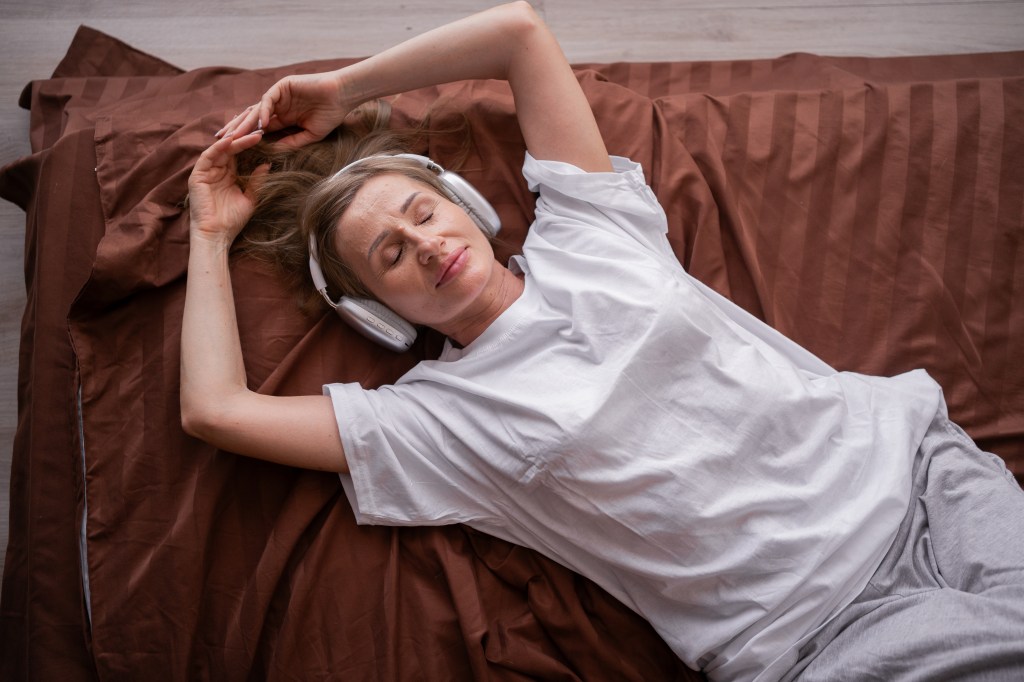 Woman relaxing and listening to music using headphones while lying in bed.