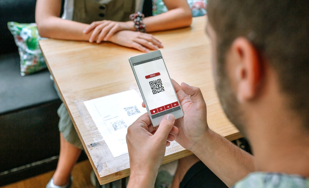 A man scanning a restaurant menu QR code on a table with his smartphone.