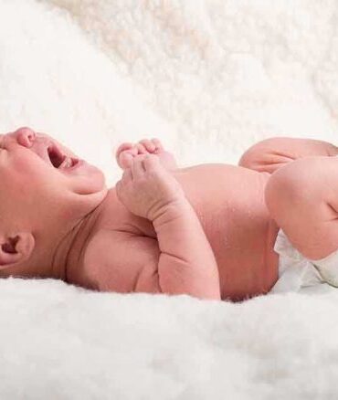 A newborn baby lying on a soft blanket, crying with a distressed expression