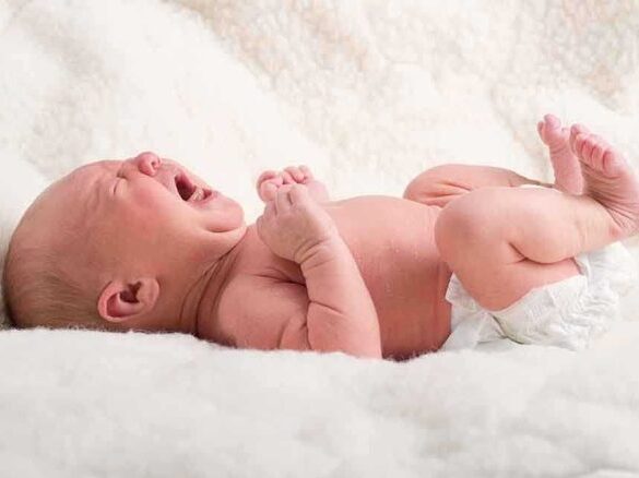 A newborn baby lying on a soft blanket, crying with a distressed expression