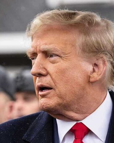 Man in suit and red tie speaking outside.