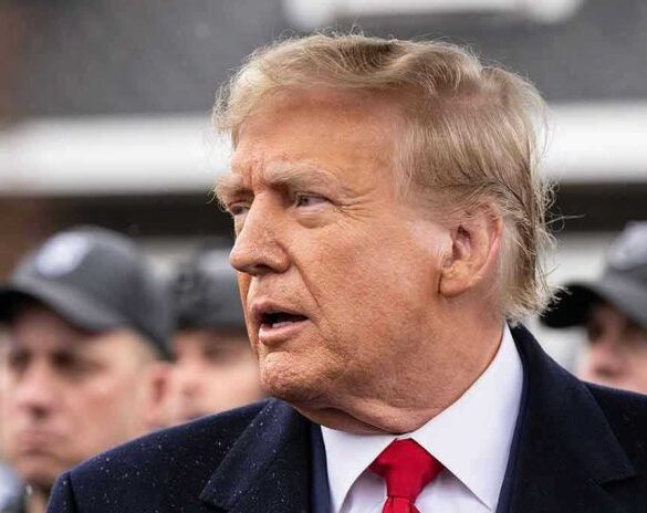Man in suit and red tie speaking outside.