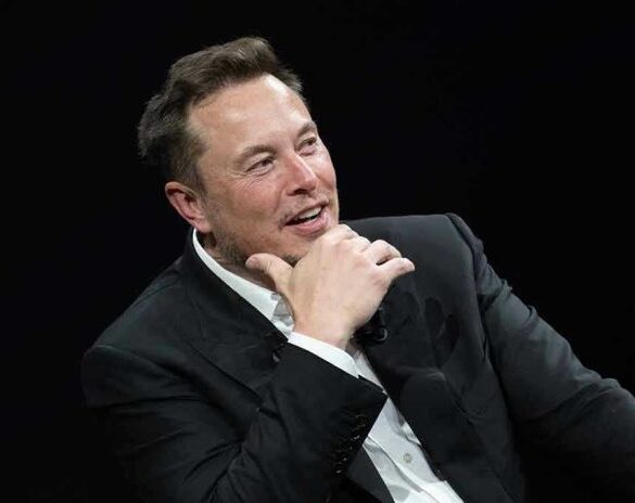 Man in suit smiling, resting chin on hand.