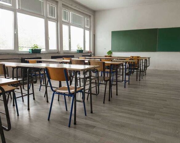 Empty classroom with desks, chairs, windows, and chalkboard.